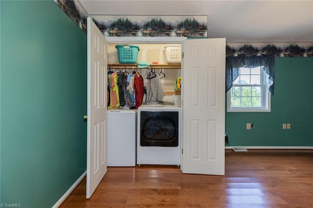 washroom featuring laundry area, wood finished floors, washing machine and clothes dryer, and baseboards