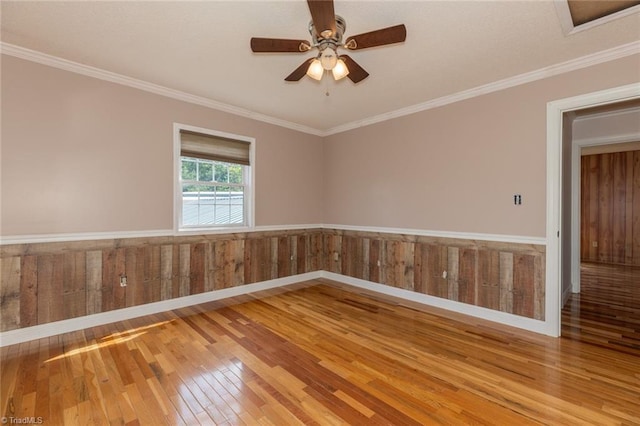 unfurnished room with wooden walls, a ceiling fan, a wainscoted wall, ornamental molding, and hardwood / wood-style floors