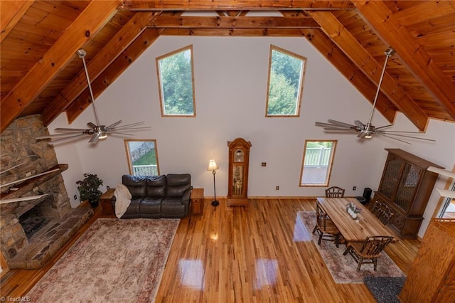 unfurnished living room with ceiling fan, beamed ceiling, wood finished floors, a fireplace, and high vaulted ceiling