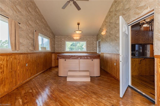 kitchen featuring lofted ceiling, wood walls, wood finished floors, wainscoting, and black refrigerator with ice dispenser