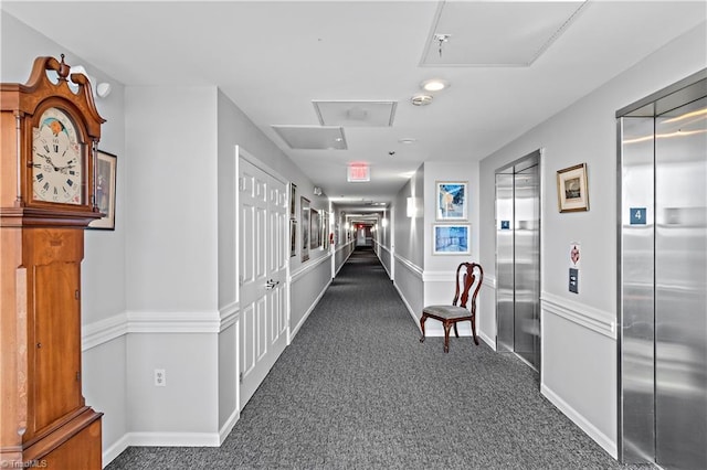 hall with elevator, baseboards, and dark carpet