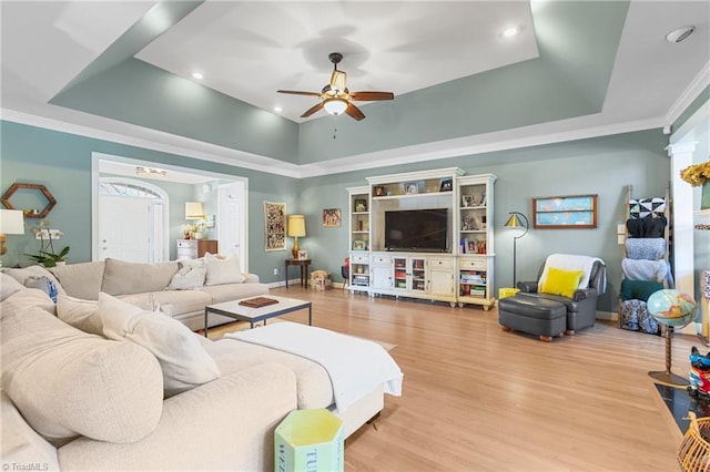 living room with a tray ceiling, ceiling fan, light hardwood / wood-style floors, and ornamental molding