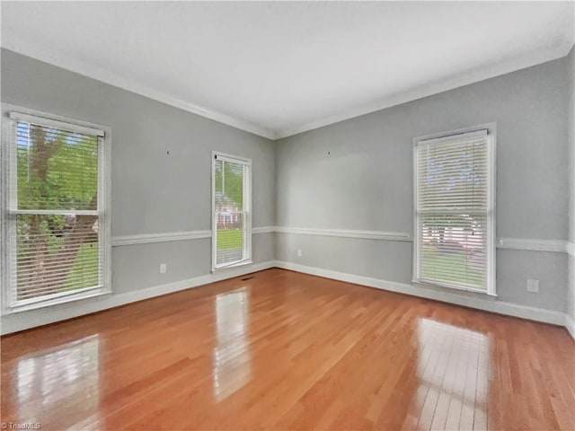 empty room featuring hardwood / wood-style flooring, baseboards, and crown molding