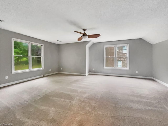 carpeted empty room with a ceiling fan, lofted ceiling, a textured ceiling, and baseboards