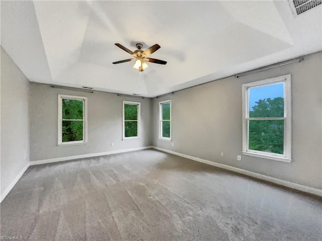 carpeted empty room with ceiling fan, visible vents, baseboards, and a raised ceiling