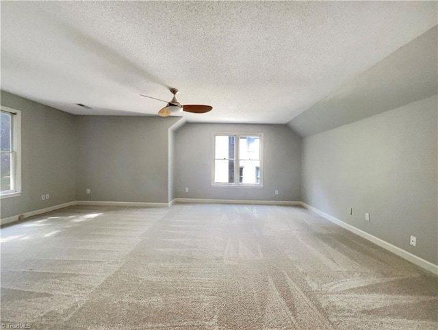 empty room with baseboards, ceiling fan, carpet, vaulted ceiling, and a textured ceiling