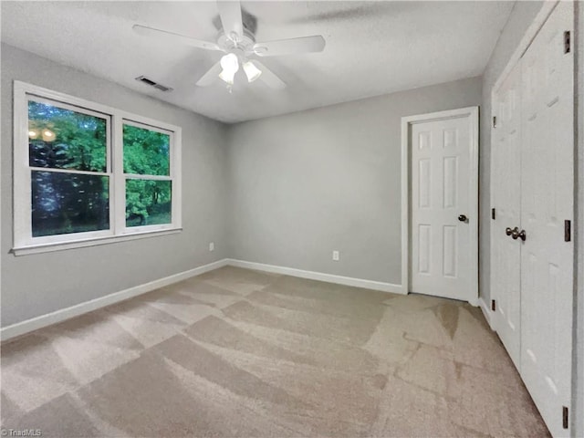 unfurnished bedroom featuring ceiling fan, light colored carpet, visible vents, baseboards, and a closet