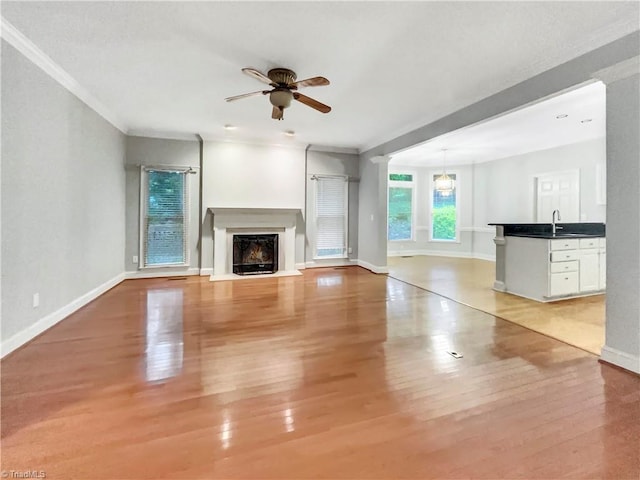 unfurnished living room with baseboards, a fireplace, a ceiling fan, and light wood-style floors