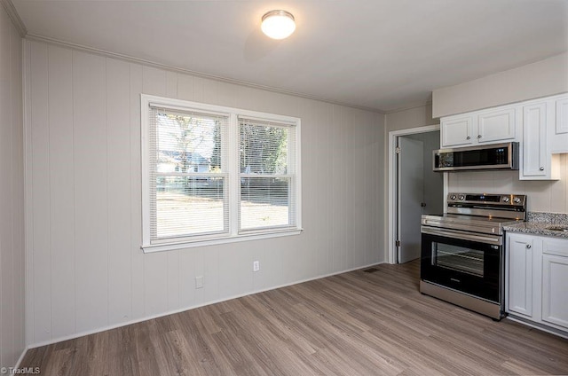 kitchen featuring white cabinetry, ornamental molding, light stone counters, stainless steel appliances, and light wood-type flooring