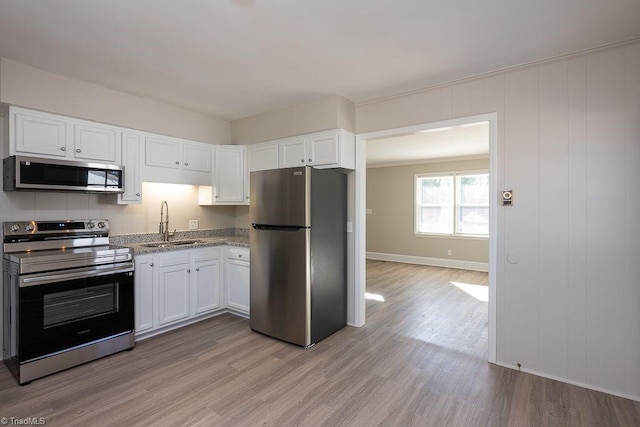 kitchen with light wood-type flooring, appliances with stainless steel finishes, sink, and white cabinets