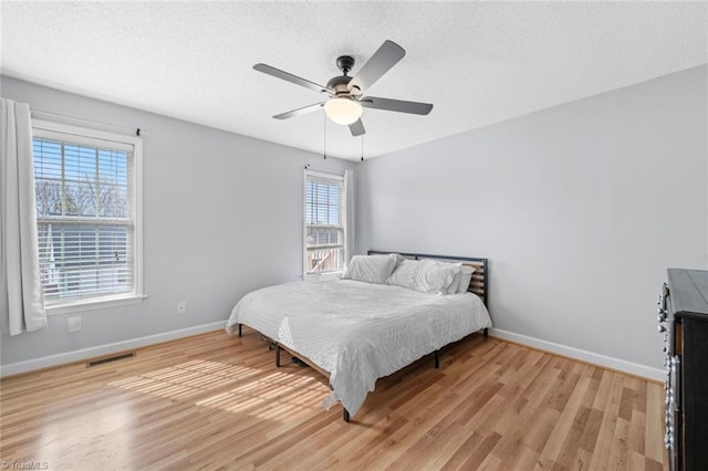 bedroom with light wood finished floors, baseboards, and a textured ceiling