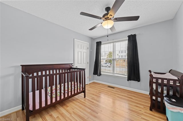 bedroom featuring a textured ceiling, ceiling fan, wood finished floors, visible vents, and baseboards