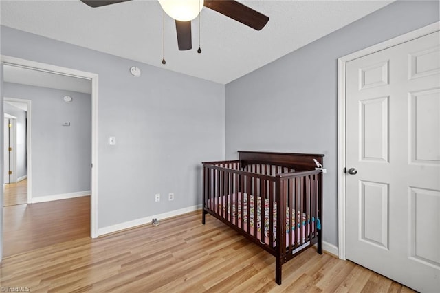 bedroom with a nursery area, a ceiling fan, baseboards, and wood finished floors