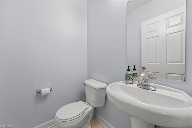 half bathroom with baseboards, a sink, and toilet