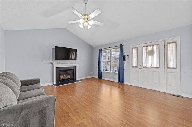 living area with baseboards, a glass covered fireplace, lofted ceiling, ceiling fan, and light wood-style floors