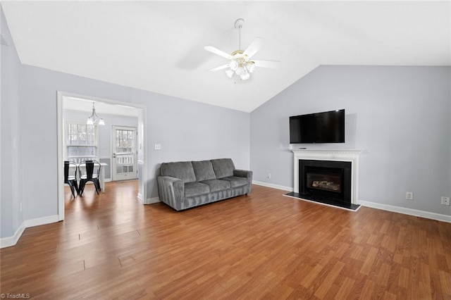 living area with a glass covered fireplace, lofted ceiling, baseboards, and wood finished floors