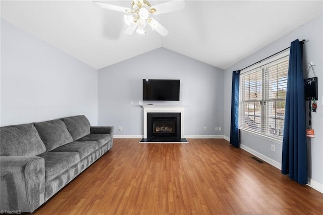 living room featuring vaulted ceiling, a fireplace with flush hearth, wood finished floors, and visible vents