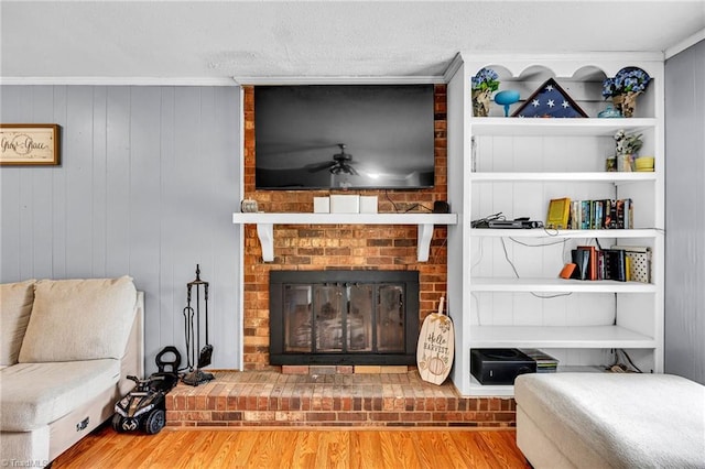 living room featuring a brick fireplace, crown molding, ceiling fan, wooden walls, and hardwood / wood-style floors