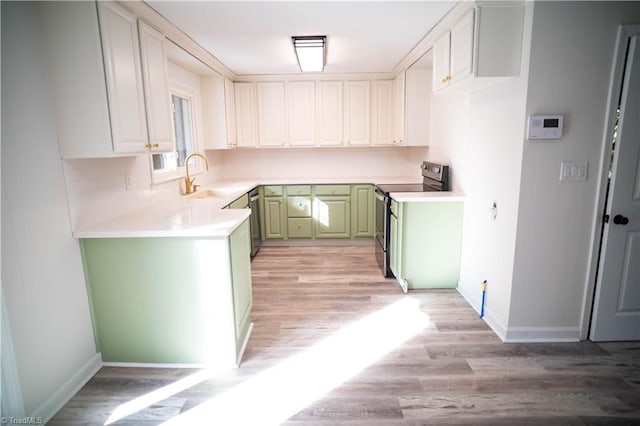 kitchen with light countertops, white cabinetry, a sink, stainless steel range with electric stovetop, and green cabinetry