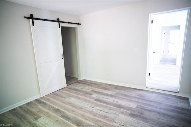 unfurnished bedroom featuring baseboards, light wood finished floors, and a barn door