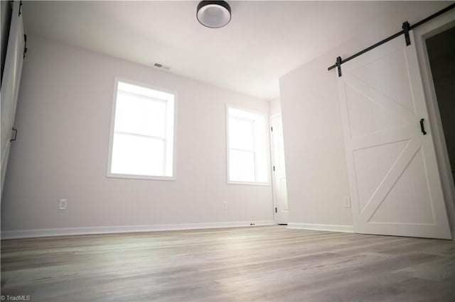 empty room with light wood finished floors, a barn door, visible vents, and baseboards