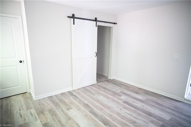 unfurnished bedroom featuring light wood finished floors, a barn door, and baseboards