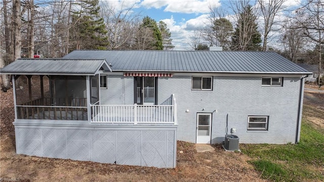 rear view of house with a sunroom, brick siding, metal roof, and central AC