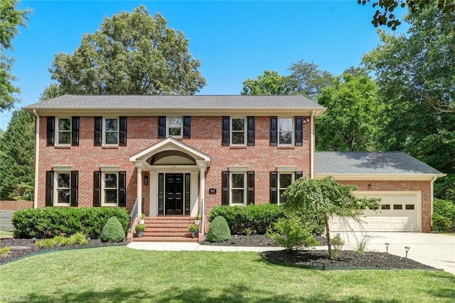 colonial home with a front yard, a garage, driveway, and brick siding