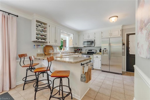 kitchen featuring stainless steel appliances, a peninsula, white cabinetry, a kitchen bar, and light countertops