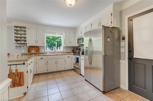 kitchen with appliances with stainless steel finishes, a sink, light tile patterned floors, white cabinetry, and ornamental molding