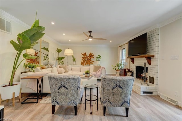 living area featuring light wood-style floors, a brick fireplace, crown molding, a ceiling fan, and recessed lighting