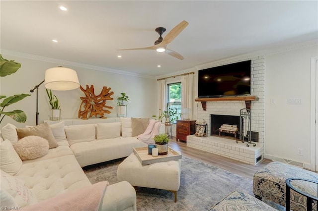 living room with a ceiling fan, crown molding, wood finished floors, a brick fireplace, and recessed lighting