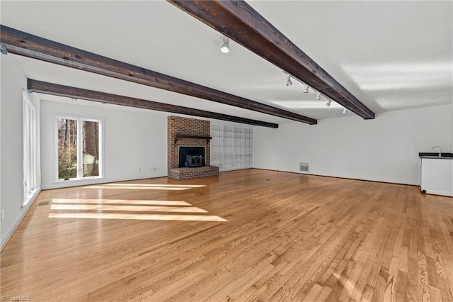 unfurnished living room with beamed ceiling, rail lighting, light hardwood / wood-style floors, and a fireplace