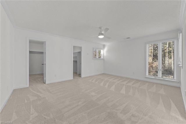 interior space featuring ceiling fan, a walk in closet, light carpet, a closet, and ornamental molding