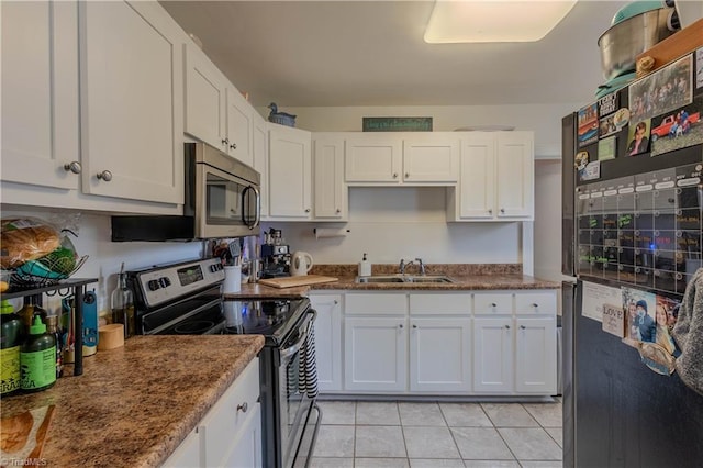 kitchen with light tile patterned flooring, appliances with stainless steel finishes, white cabinetry, sink, and dark stone countertops