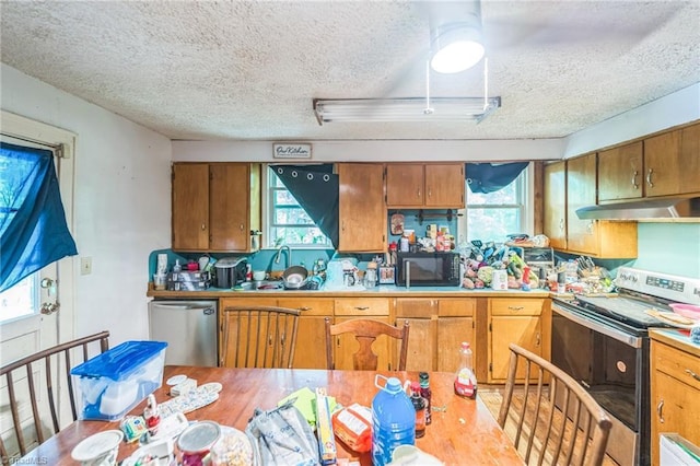 kitchen featuring appliances with stainless steel finishes, under cabinet range hood, a textured ceiling, plenty of natural light, and brown cabinets