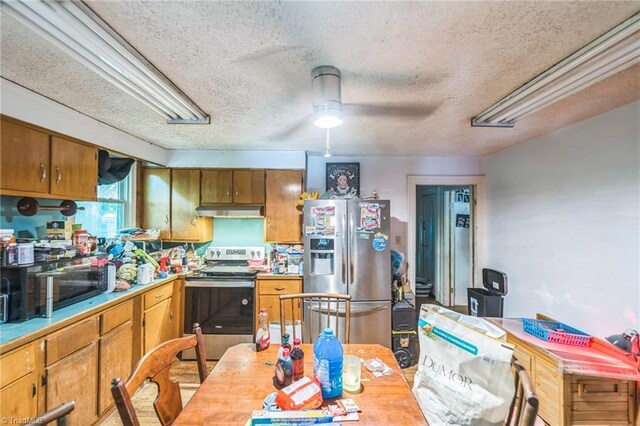 kitchen with appliances with stainless steel finishes, under cabinet range hood, brown cabinetry, light countertops, and a textured ceiling