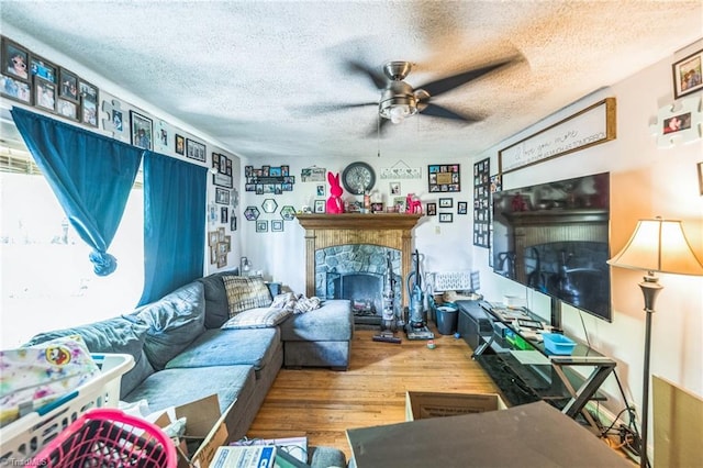 living area with ceiling fan, wood finished floors, a fireplace, and a textured ceiling