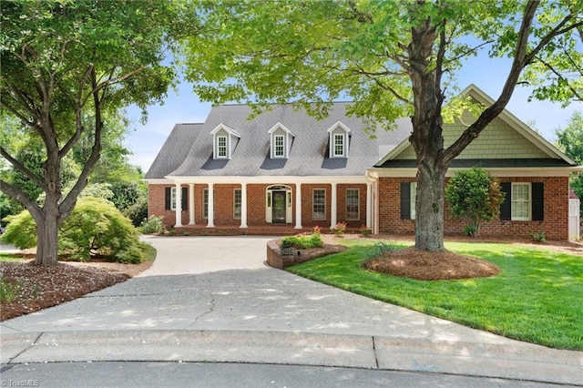 cape cod house featuring a porch, a front lawn, and brick siding