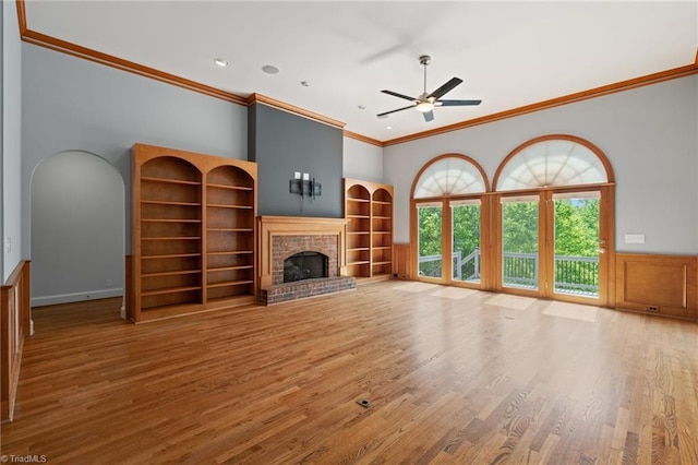 unfurnished living room with crown molding, a high ceiling, a brick fireplace, a ceiling fan, and wood finished floors