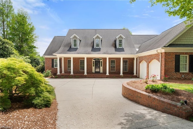 new england style home featuring covered porch, brick siding, driveway, and a garage