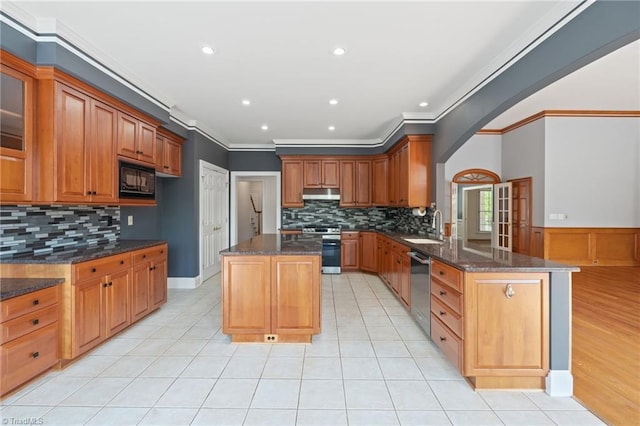 kitchen with crown molding, dark stone counters, arched walkways, a sink, and stainless steel appliances