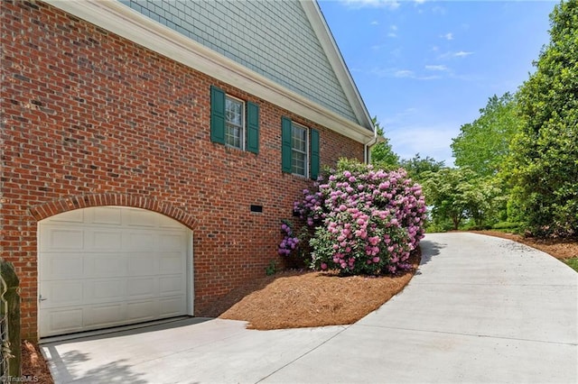 view of property exterior featuring brick siding, driveway, and a garage