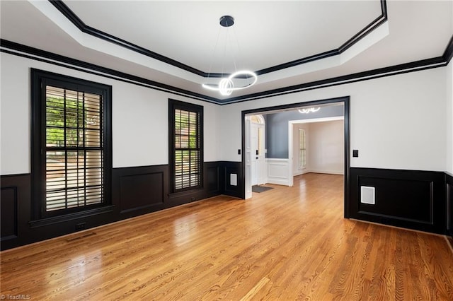 unfurnished room with a raised ceiling, ornamental molding, wainscoting, and a notable chandelier