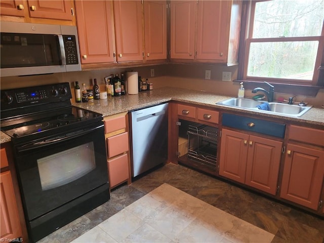 kitchen with brown cabinetry, light stone counters, stainless steel appliances, and a sink