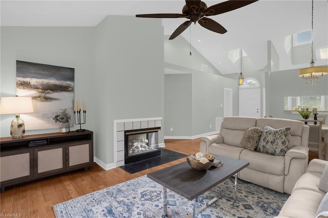 living room with hardwood / wood-style flooring, a tile fireplace, vaulted ceiling, and ceiling fan with notable chandelier