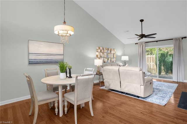 dining area featuring ceiling fan with notable chandelier, wood-type flooring, and high vaulted ceiling