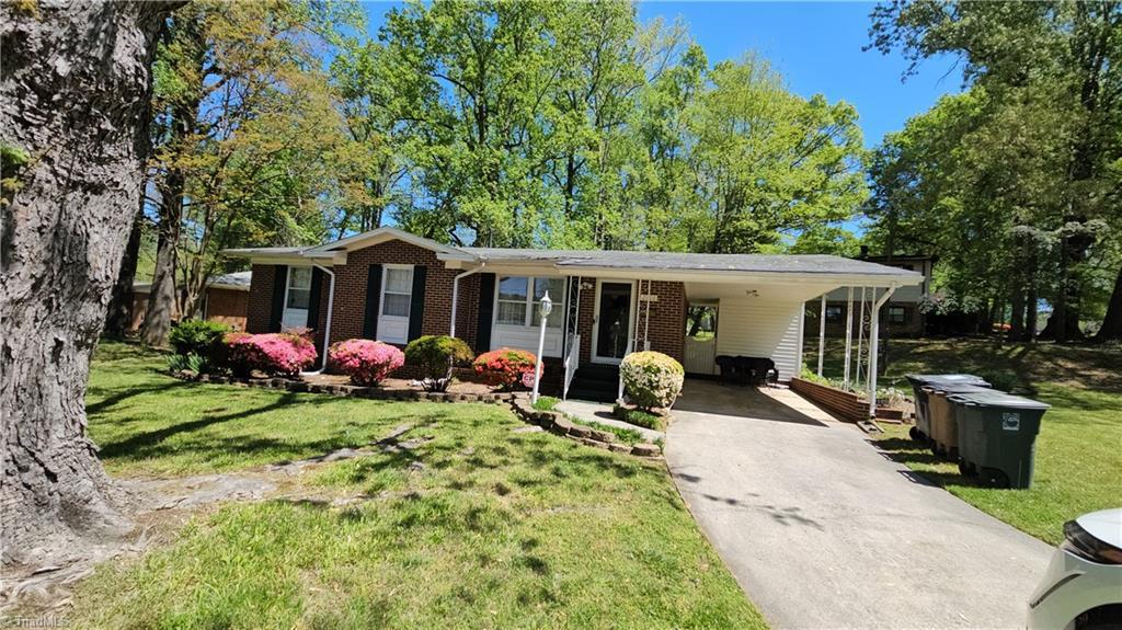 ranch-style home featuring a front lawn, driveway, a carport, entry steps, and brick siding