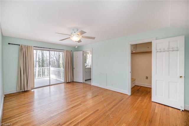 unfurnished bedroom with ensuite bathroom, a spacious closet, access to outside, ceiling fan, and light wood-type flooring