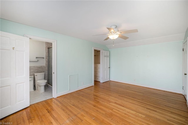 unfurnished bedroom with ceiling fan, ensuite bath, and light wood-type flooring